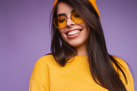 Smiling Woman in Yellow Outfit With Sunglasses Against Vibrant Purple Backgroundの写真素材