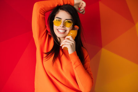 Cheerful Woman in Orange Outfit Posing with a Colorful Background and Drinkの写真素材