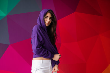 Young Woman in Purple Hoodie Smiling Against Vibrant Colorful Geometric Backgroundの写真素材