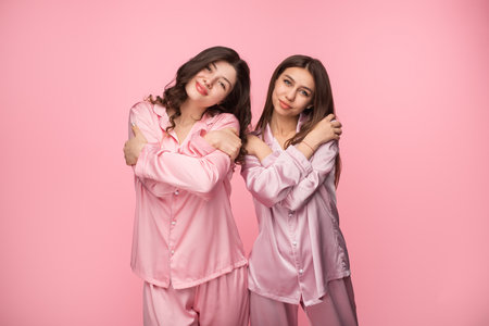 Two Women in Pink Pajamas Embracing Against a Pastel Backgroundの写真素材