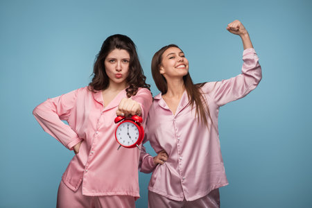 Two Women in Pink Pajamas Holding Alarm Clock and Celebrating Morningの写真素材