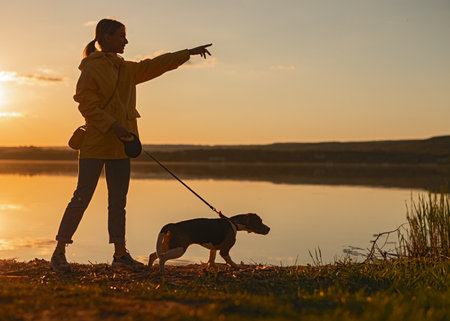 Woman Walking Her Dog at Sunset by a Calm Lakeの写真素材