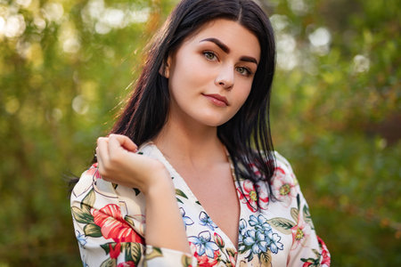 Elegant Woman Posing Outdoors in Floral Dress During Sunny Dayの写真素材