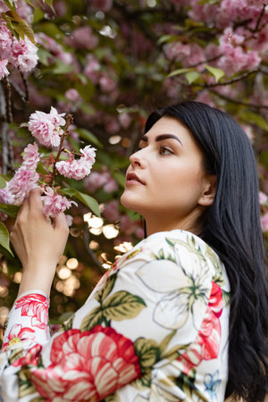 Beautiful Woman Admiring Cherry Blossoms in a Blooming Spring Gardenの写真素材
