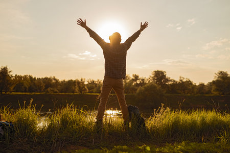 Man Raising Arms in Freedom Amidst Scenic Sunset Landscape Outdoorsの写真素材