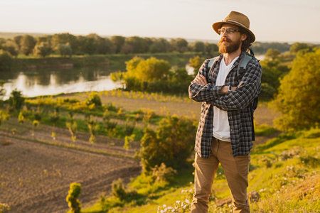 Bearded Man in Rustic Hat Enjoying Scenic Rural Landscape Outdoors at Sunsetの写真素材