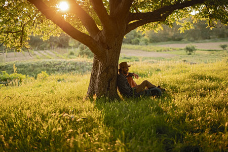 Tranquil Man Relaxing Under Tree at Sunset in a Rural Landscapeの写真素材