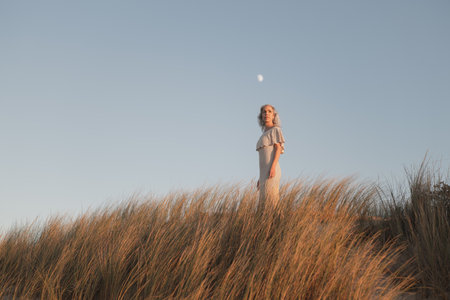 Serene Woman Standing in Tall Grasses Under a Clear Sky at Duskの写真素材