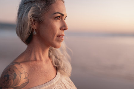 Serene Woman With Tattoo Gazing at Ocean During Sunsetの写真素材