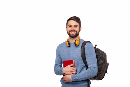 Smiling Male Student Holding Book With Backpack and Headphones Isolated on Whiteの写真素材
