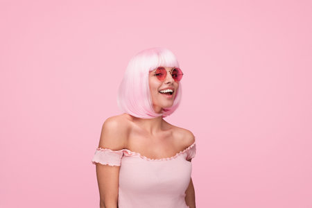 Young Woman Wearing Pink Wig and Sunglasses on a Vibrant Colorful Backgroundの写真素材