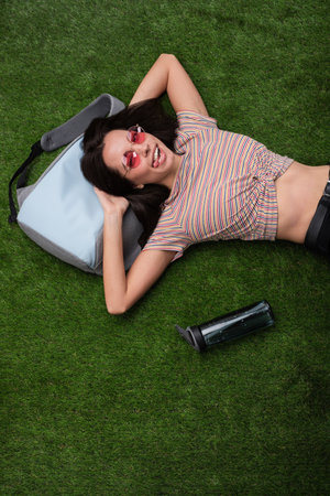 Smiling Woman Relaxing on Grass With Sunglasses and a Backpackの写真素材
