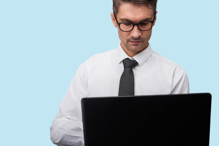 Professional Businessman Working on a Laptop Against a Light Blue Backgroundの写真素材