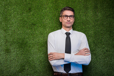 Confident Businessman in Formal Attire Standing Against Green Grass Backgroundの写真素材