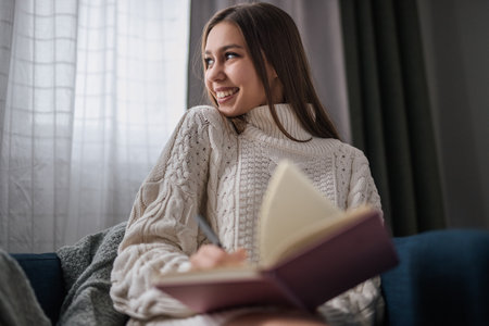 Smiling Young Woman Writing in Notebook at Home During Daytimeの写真素材