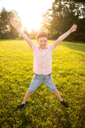 Boy Jumping Happily Outdoors in a Sunny Green Park During Golden Hourの写真素材