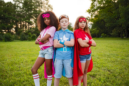 Three Kids Dressed As Superheroes Standing Outdoors in a Green Fieldの写真素材