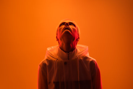 Person in Hooded Jacket Illuminated by Vivid Orange Lighting From Belowの写真素材