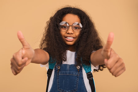 Smiling Girl Showing Thumbs-Up Gesture Wearing Glasses and Denim Overallsの写真素材
