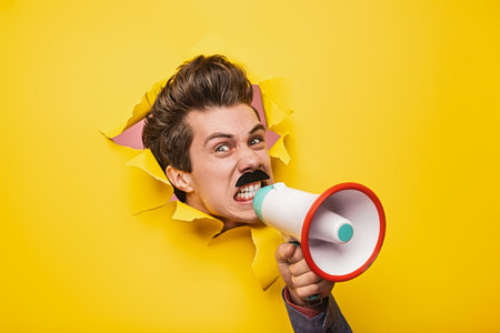 Man Shouting Through Megaphone Against Bright Yellow Background for Communication Conceptの写真素材