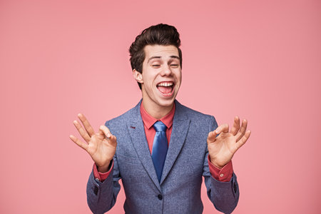 Smiling Young Man in Suit on Pink Background Gesturing Happinessの写真素材
