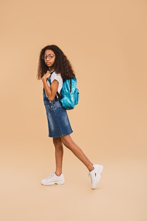 Young Girl Standing Confidently with Backpack on Neutral Beige Backgroundの写真素材