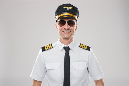 Confident Pilot in Uniform with Sunglasses Smiling Against a Neutral Backgroundの写真素材