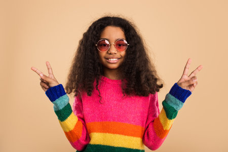 Smiling Girl in Colorful Sweater Showing Peace Signs with Sunglassesの写真素材