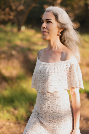 Serene Woman With Gray Hair Walking Through Sunlit Forest Pathの写真素材