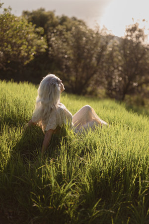 Woman Relaxing in Lush Green Field During Golden Hour Sunsetの写真素材