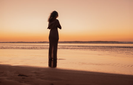 Solitary Woman Standing on Beach at Sunset Contemplating the Horizonの写真素材
