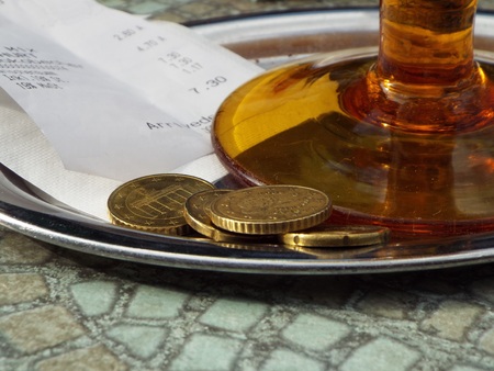 Tipping on a tray located under a brown glass a receipt alongwith loose change.の写真素材