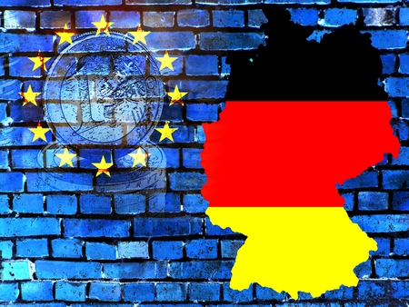 The map of Germany in the colors of the national flag in front of a bluish brick wall with the European circle of stars. Translucent: a Euro coin.の写真素材
