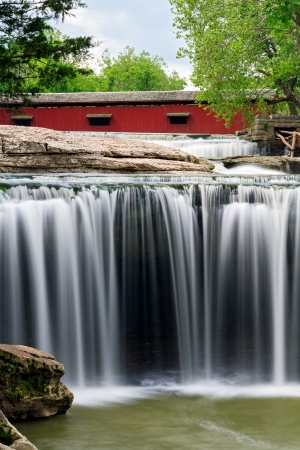 The red Cataract Covered Bridge spans Indiana's Mill Creek just upstream from beautiful Upper Cataract Falls.の写真素材