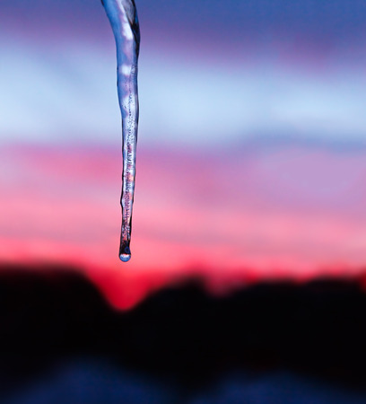 An icicle is backed by a colorful winter sunset sky の写真素材