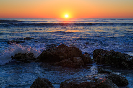 The sun rises over the Atlantic Ocean with waves breaking on a Florida beach covered with coquina...