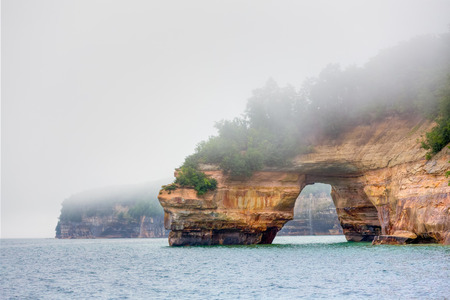 Fog hangs over a huge rock portal known as Lovers Leap on Michigan's Lake Superior coast at Pictured Rocks National Lakeshore.の写真素材