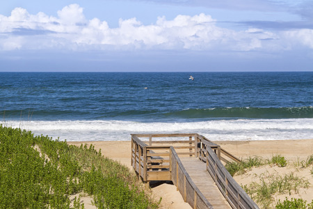 Waves break on a sandy North Carolina beach with a wooden boardwalk and deck on the dunes.の写真素材