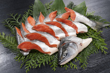 raw salmon fish on a wooden board with green leaves on a black backgroundの写真素材