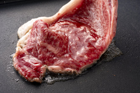Raw beef steak on a black frying pan, closeup, horizontalの写真素材
