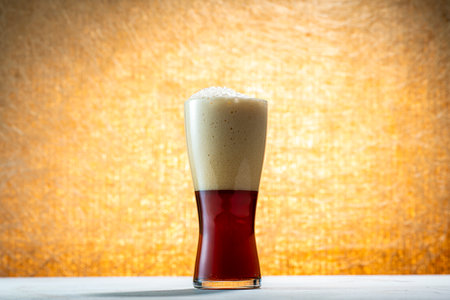 Glass of dark beer with foam on a table and yellow backgroundの写真素材