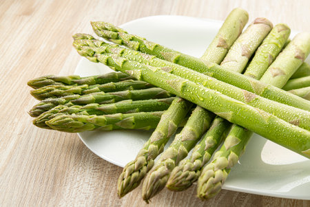 Bunch of fresh green asparagus on white plate on wooden tableの写真素材
