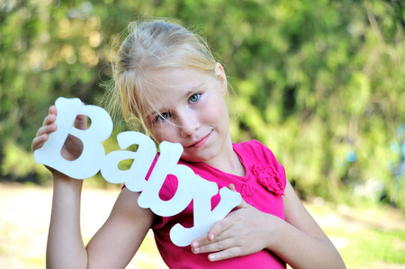 Young girl hold wooden decoration handmade word baby near faseの写真素材