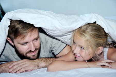 Smiling father and his daughter having fun lying on a bed looking each otherの写真素材