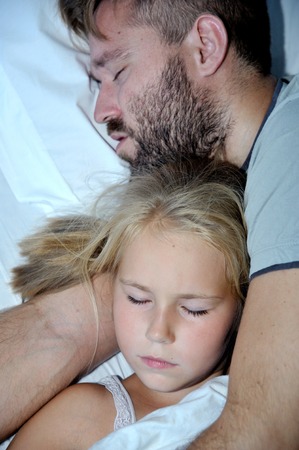 Dad and little blonde girl sleeping together on bedの写真素材