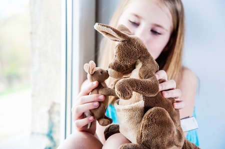 beautiful girl 8 years old playing with her toy big and little kangaroos near windowの写真素材