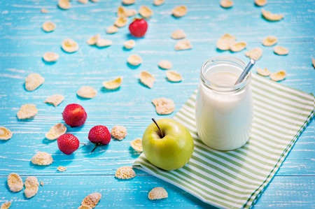 Jar of milk and green apple in the striped napkin on the table. Corn flakes with strawberry scatter.の写真素材
