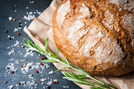 A loaf of bread with rosemary salt and pepper on paper closeup