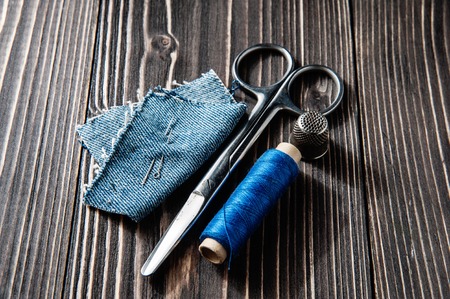 Jeans, blue thread, needle and scissor on wooden background dark tone - rustic style, top viewの写真素材