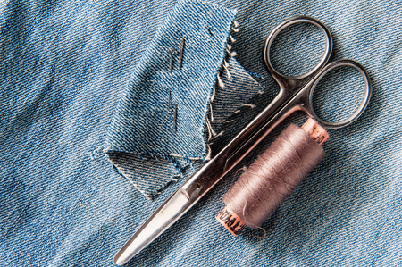Sewing kit from pink threads, scissor and needle on jeans backround